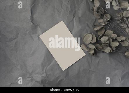 Kartenleerpapier für Modellschablone auf zerknittertem grauem Papier mit trockenem Eukalyptus-Stieldekor. Stockfoto