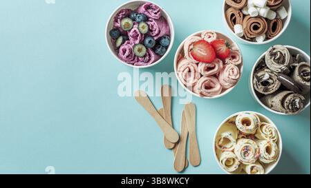 Gerollte Eiscremes in Kegelbechern auf blauem Hintergrund. Verschiedene Eisrollen von oben oder flach. Thailändisches Eis mit Kopierraum für Text oder Stockfoto