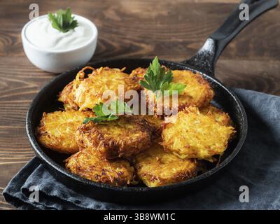 Kartoffeln Pfannkuchen Latkes, Flapjacks, Kartoffelbraun oder kartoffelvada mit weißem griechischem Joghurt oder Sauerrahm auf braunem Holztisch. Kopierbereich für Text Stockfoto