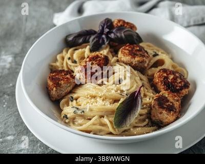 Zucchini Parmesan Fleischbällchen mit Pasta Carbonara in weißer Platte auf grauem Hintergrund. Nahaufnahme von cremigem Carbonara mit Kopierraum links Stockfoto