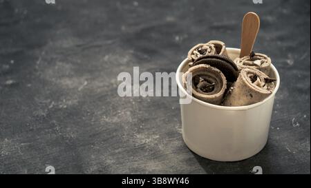 Gerolltes Eis mit in Kegelbecher auf dunklem rustikalem Hintergrund. Eiswürfelrollen mit Keksen Schokolade Sandwich Cookies. Gerolltes Eis im thailändischen Stil mit Polizist Stockfoto