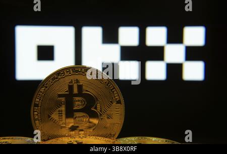 Dhaka, Bangladesch - 04. April 2025: Nahaufnahme von Bitcoin-Münzen mit dem OKX-Logo auf einem Bildschirm im Hintergrund Stockfoto