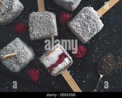 Hausgemachte raw lamington Eis erscheint auf dunklem Hintergrund. Australische süße Nachspeise lamington mit Chia und Himbeeren Marmelade, Schokolade und Kakao. Stockfoto