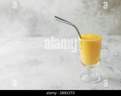 Gelbe mango Joghurt oder Smoothie auf grauem Zement Hintergrund mit Kopie Raum gelassen. Gelbwurz Lassie oder Lassi in Glas mit Metall Strohhalme Stockfoto