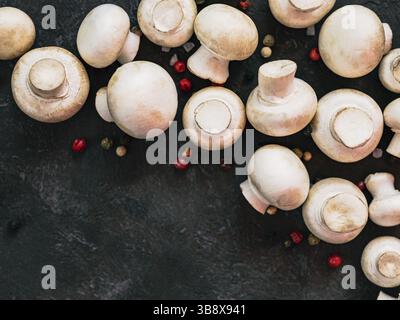Mini-Champignons mit Kopierraum am linken Rand. Rohe ganze Pilze auf schwarzem Hintergrund, Kopierraum. Draufsicht oder flache Lagen Stockfoto