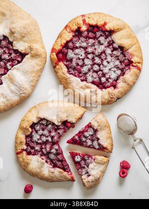 Drei perfekte Himbeer-Galetten. Köstliche rustikale hausgemachte Tarte mit gefrorenen oder frischen Himbeeren, Marmorhintergrund. Schöne Galetten mit Raspberr Stockfoto