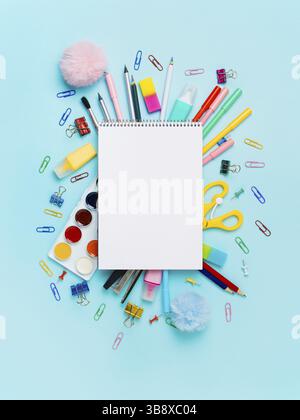 Notizbuch mit stationären Objekten auf blauem Hintergrund. Leeres weißes Papierblatt mit Notizblock oder Skizzenbuch über Schulbedarf, isoliert auf blau. Vertikal. Stockfoto