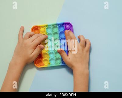 Kinder Hände spielen popit Spielzeug, Draufsicht über zwei Schatten blauen Hintergrund. POPIT auf blauem Hintergrund, Kopierbereich. Beliebte Silikon bunte Anti-Stress Pop it Stockfoto