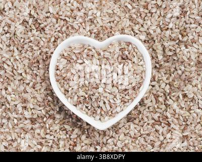 Roter Reis in herzförmiger Schüssel auf Reishintergrund. Kopierbereich. Draufsicht oder flache Lagen Stockfoto