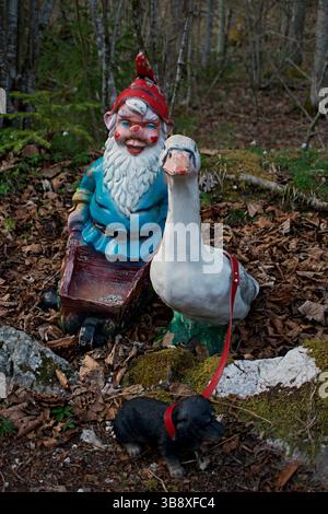 Farbenfrohe Garden Gnome Statue mit Gänse und Dachshund Figuren im Wald Stockfoto