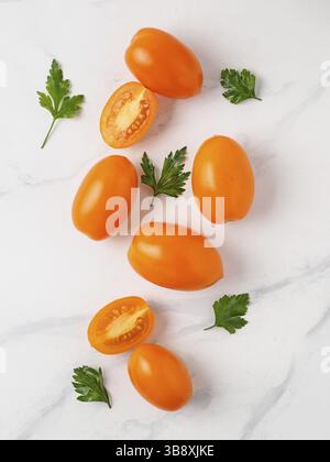 Orange Tomaten auf weißem Marmortisch. Gelb oder Orange Tomaten mit zwei halben aufgeschnittenen Tomaten und frischer Petersilie. Top View oder flach. Vertikale Stockfoto