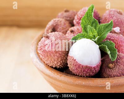 Litschi-Frucht in Tonplatte auf hölzernem Hintergrund Nahaufnahme Stockfoto