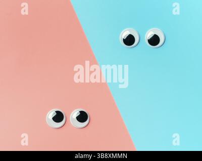 Schöne Augen auf blauem und rosa Hintergrund. Draufsicht oder flach liegend. Kunststoff Spielzeug Augen auf türkisfarbenem Hintergrund Stockfoto