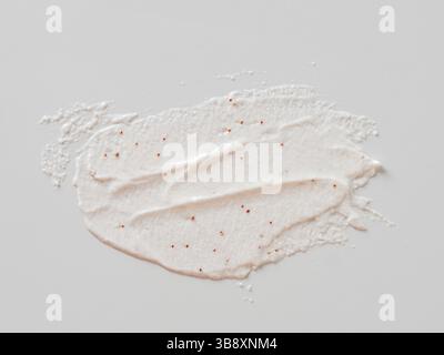 Flecken auf weißem Hintergrund. Kosmetisches Peeling mit Textur für Gesicht und Körper mit roten Schleifpartikeln in pastellrosa Farbe. Peeling-Körper Stockfoto