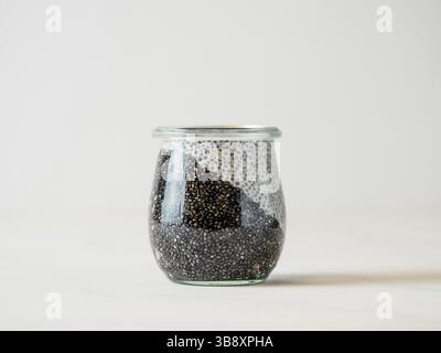 Gesundes Frühstück Konzept und Idee - zwei Farben chia Pudding auf weißen Tischplatte. Glas Glas mit schwarzer Kohle und weiße vegane Milch chia Pudding. Kopieren Stockfoto