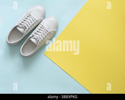 Weißes Leder Sneakers an blauen und gelben Hintergrund. Paar trendige Mode weißen Sport Schuhe oder Turnschuhe mit Kopie Platz für Text auf bunten backgr Stockfoto