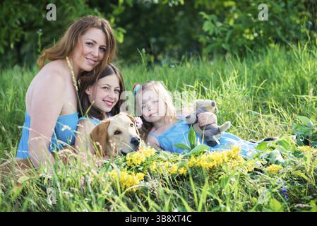 Mutter, zwei Töchter und ein Hund, der auf dem Gras im Garten sitzt Stockfoto