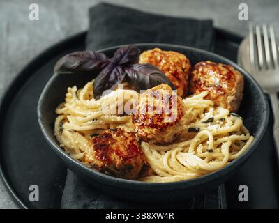 Zucchini Parmesan Fleischbällchen mit Pasta Carbonara in schwarzem Craft Teller auf grauem Hintergrund. Nahaufnahme von cremigem Carbonara mit Kopierraum links Stockfoto