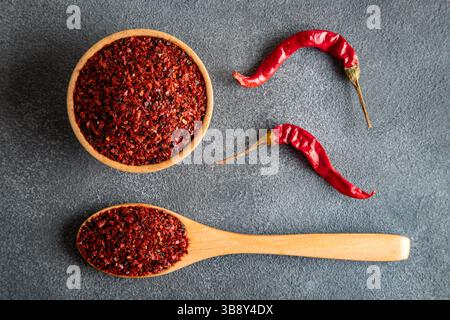 Rote Pfefferflocken. Rote Chilischoten in Holzschale auf schwarzem Hintergrund. Getrocknete Chilischoten Stockfoto