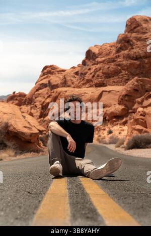 Mann sitzt auf den gelben Mittelstreifen mitten auf der Straße im Valley of Fire State Park. Porträts im Red Rock Park in Arizona. Stockfoto