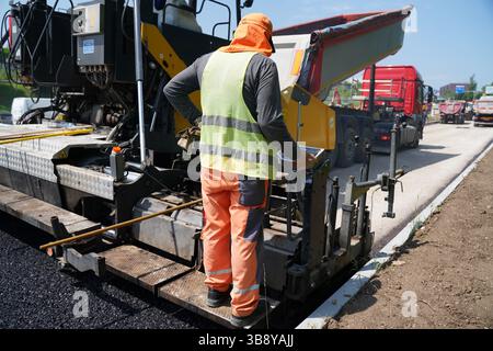 Bauarbeiter, der Asphaltfertiger auf der Straßenbaustelle betreibt Stockfoto