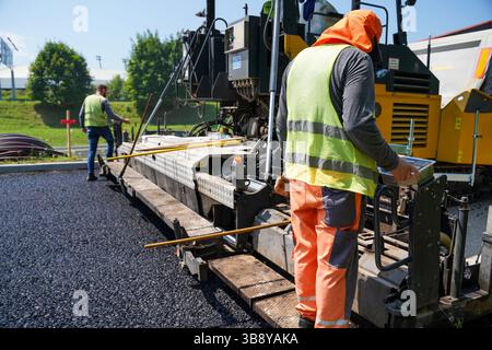 Bauarbeiter, die Asphaltfertiger auf der Straßenbaustelle betreiben Stockfoto