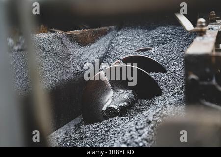 Detaillierte Nahaufnahme der Flügelräder eines Asphaltfertigers, die die kritischen Komponenten für eine gleichmäßige Verteilung und reibungslose Anwendung darstellen Stockfoto