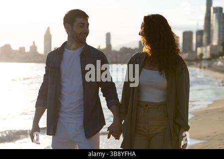Ein Paar hält Hände und lächelt am Strand bei Sonnenuntergang. Lifestyle. Urlaub. Stockfoto