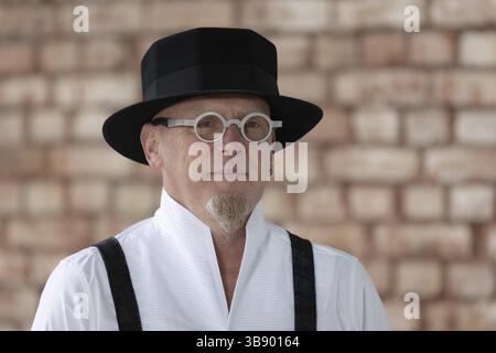 Mann mit markanter Brille und Hut vor Backsteinhintergrund, traditionell gekleidet, inszenierte Porträtaufnahmen, München, Bayern, Deutschland, Europa Stockfoto