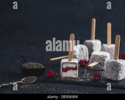 Hausgemachte raw lamington Eis erscheint auf dunklem Hintergrund. Australische süße Nachspeise lamington mit Chia und Himbeeren Marmelade, Schokolade und Kakao. Stockfoto