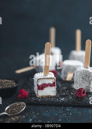 Hausgemachte raw lamington Eis erscheint auf dunklem Hintergrund. Australische süße Nachspeise lamington mit Chia und Himbeeren Marmelade, Schokolade und Kakao. Stockfoto