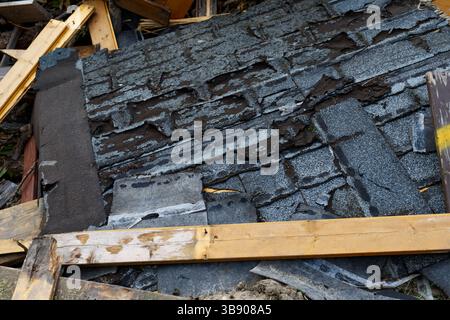 Abblätternde, verschlissene Asphaltschindeln zeigen eine Verschlechterung der Dachoberfläche. Verwittert und beschädigt zeigen die Gürtelrose Zeichen von Alter und Vernachlässigung Stockfoto