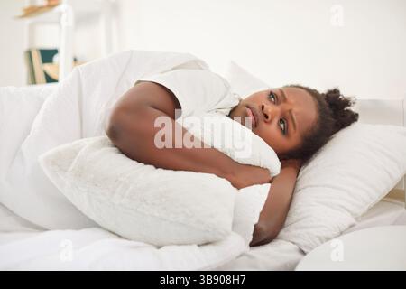 Verärgert frustrierte junge afroamerikanische Frau Kissen liegt allein im Bett, schwarze Dame fühlt sich einsam Stockfoto