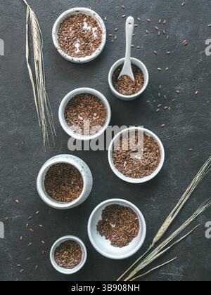 Leinsamen und trockenes Roggenohr auf dunklem Hintergrund. Set aus kleinen Schüsseln mit Bio-Flachssamen oder Leinensamen. Leinsamen sind reich an Omega-3-Fettsäuren. Vert Stockfoto