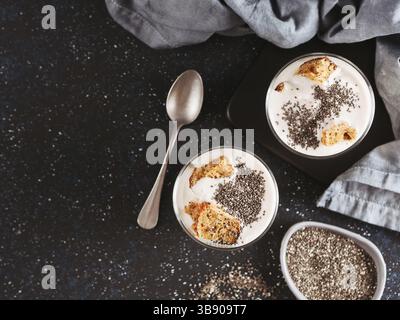 Keine gebackene Käsetorte Dessert mit zerdrückte Karotten Kekse und Chia Samen in Glas Glas auf dunklem Hintergrund. Ideen und Rezepte für gesundes Frühstück. Cop Stockfoto