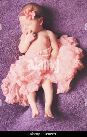 Neugeborenes hübsches Baby-Mädchen im rosa Tutu-Kleid schläft auf dem lila Textil Stockfoto