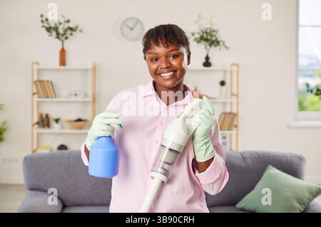 Porträt einer afroamerikanischen Frau, die während der Reinigung Vakuum und Spray hält Stockfoto