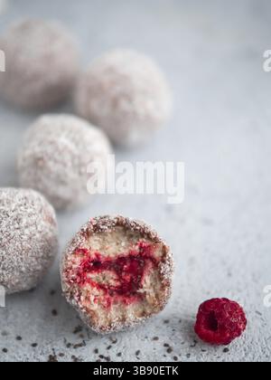 Raw vegan Lamington bliss Kugeln mit Himbeeren chia Stau auf grauem Hintergrund. Keine gebackene Gesund vegan süße Nachspeise Idee und Rezept. Kopieren Sie Raum für Tex Stockfoto