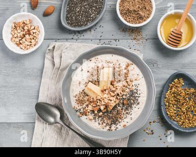 Über Nacht Hafer in der Schüssel und Zutaten - Banane, LSA, Chia Samen, Mandeln, Honig und Pollen auf grau Holztisch Hintergrund. Gesundes Frühstück Haferflocken Stockfoto