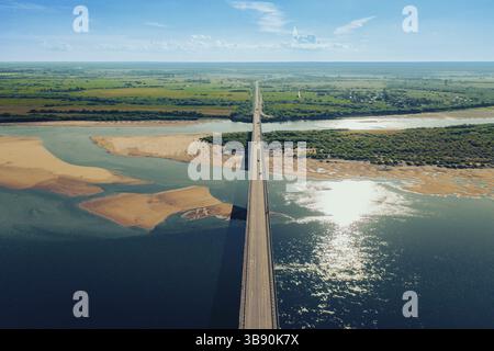 Luftaufnahme von Autos, die auf einer Brücke über den Fluss und am sandigen Flussufer bei Sonnenuntergang fahren. Atemberaubende ästhetische 4K°-Draufsicht mit wunderschöner Küste mit Dun Stockfoto