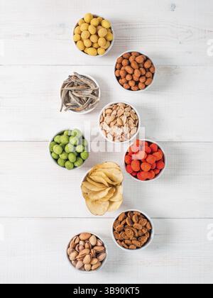 Auswahl an verschiedenen Snacks für Bier, Wein, Party. Erdnüsse in Kokosglasur, grüne Vasabi, rote scharfe Chili, Gelbkäse und Chips, Pistazien Stockfoto