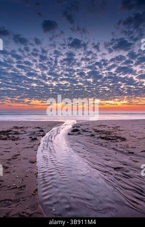 Sonnenuntergang am Strand von Katwijk aan Zee. In den Sand, in den das Wasser aus dem Meer fließt, wurde eine Rille gegraben Stockfoto