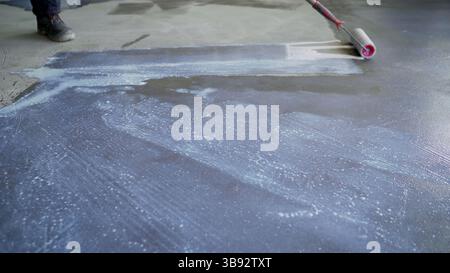 Bauarbeiter, der Epoxidharz mit einer Walze auf einem Betonboden aufträgt, um die Abdichtung zu gewährleisten und die Haltbarkeit der Oberfläche zu verbessern Stockfoto