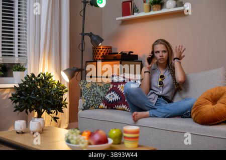 Eine junge Frau, die einen lebhaften Anruf führt, während sie in ihrem gemütlichen Wohnzimmer sitzt Stockfoto