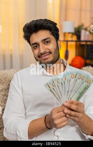 Indischer Mann zu Hause, der Bargeld zählt, sein Budget sorgfältig überlegt und zukünftige Ausgaben plant. Ein Araber sitzt auf dem Sofa und konzentriert sich auf Geldmanagement und durchdachte Finanzentscheidungen Stockfoto