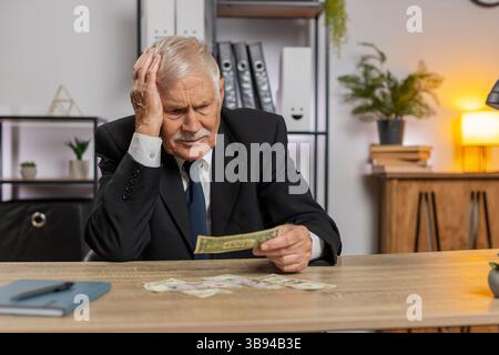 Kaukasischer Senior-Geschäftsmann Freelancer zählt Bargeld zu wenig Geld. Finanzkrise. Konkurs. Armut und Elend. Großvater im Anzug sitzt am Tisch im Büro. Stockfoto