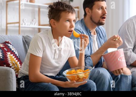 Fröhliche Familienessen, während man zuhause Fußballspiele auf dem Sofa ansieht Stockfoto
