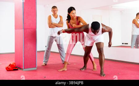 Selbstverteidigungstrainer lehrt asiatische Frau Stärke Techniken in Sporthalle Stockfoto