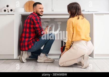 Junge Frau und Klempner reparieren Spülbecken in der Küche Stockfoto