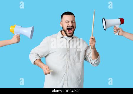 Junger Mann, der Trommelstöcke hält und weibliche Hände mit Megaphonen auf blauem Hintergrund. Künstler als Outlaw Day Stockfoto